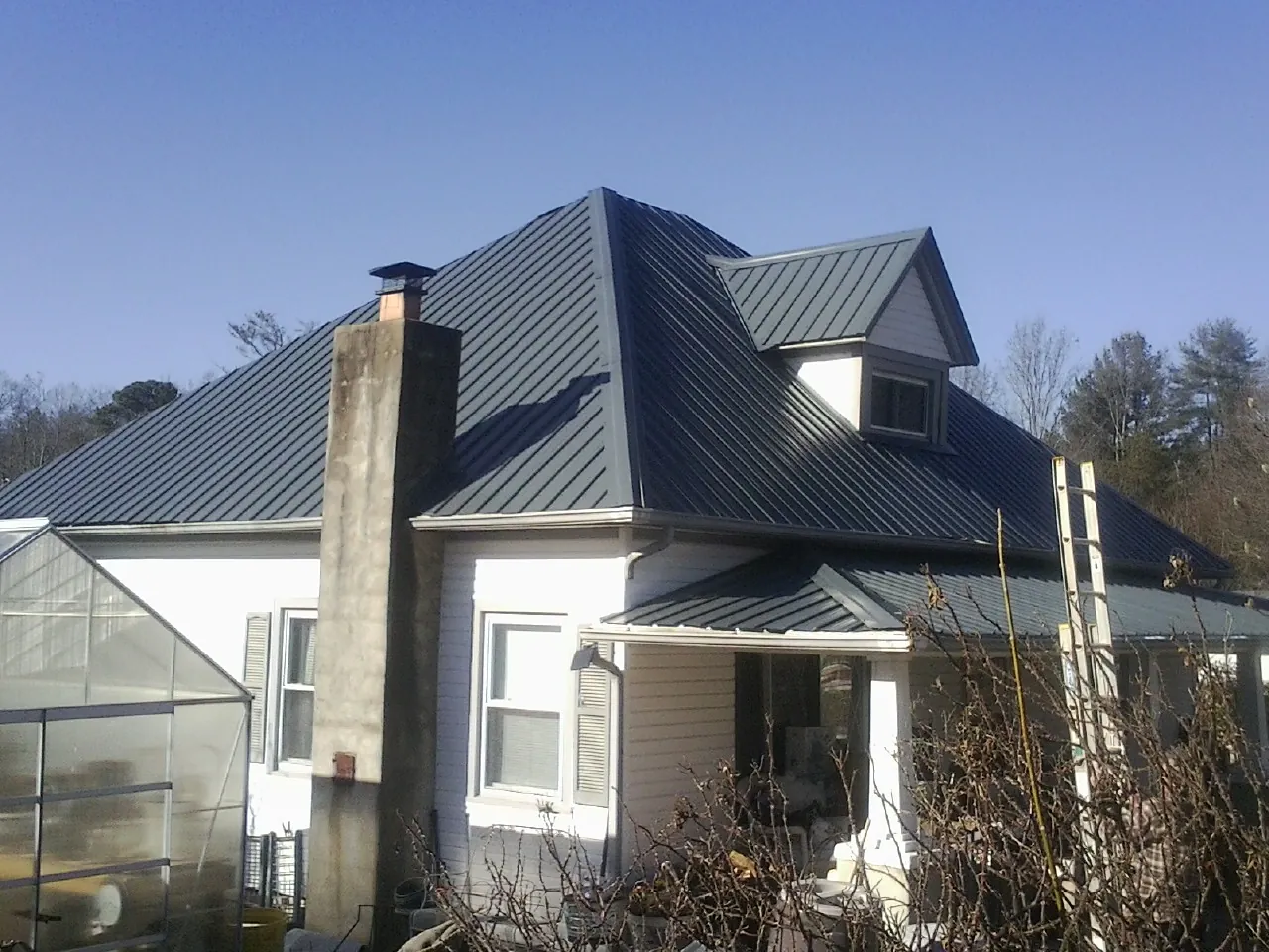 Dark blue standing seam metal roof on a white farmhouse with dormer — Slate & Tile Roof Repair by Roofing Brothers in Ripplemead