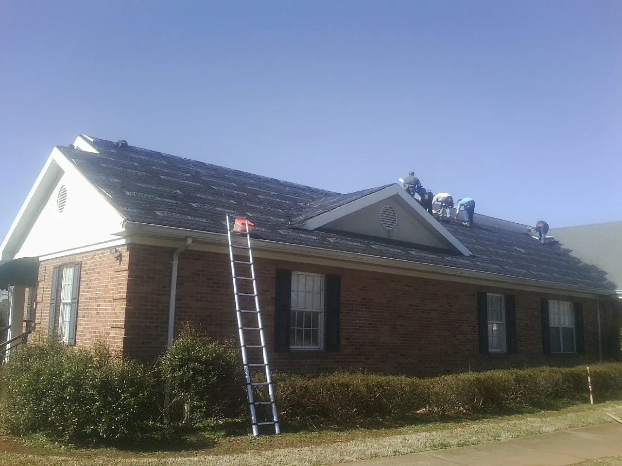 Crew tearing shingles off a brick ranch roof with a ladder set — Emergency Roof Repair work by our crew in Ripplemead
