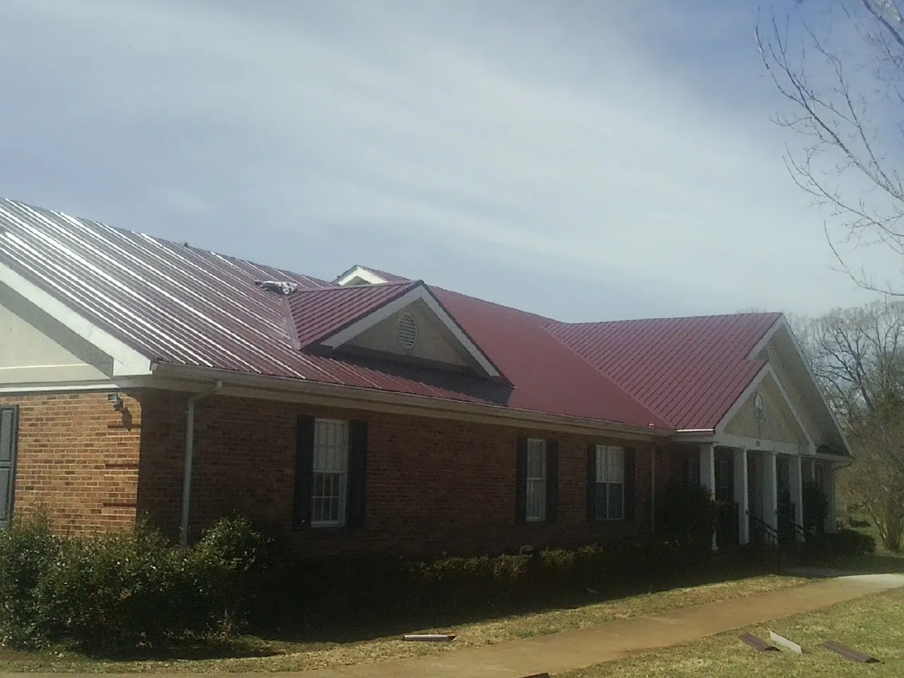 Red metal roof with gabled entries on a long brick building, from a Hail Damage Roof Repair job in Ripplemead