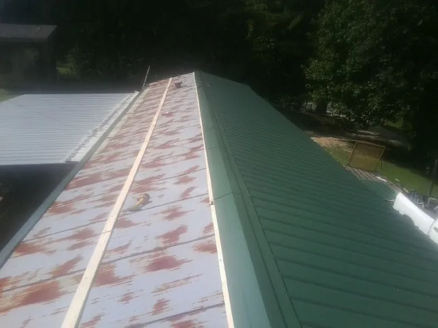 Old rusted panels beside newly installed green metal roofing — Wind Damage Roof Repair by Roofing Brothers in Ripplemead