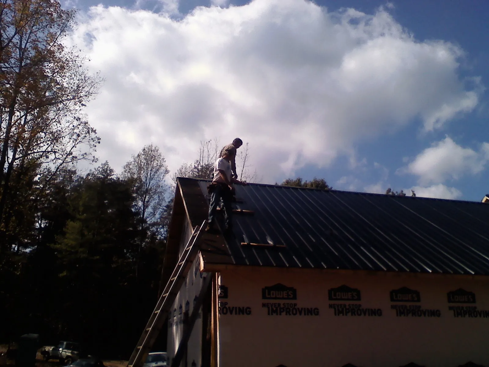 Roofer fastening dark metal panels high against a cloudy sky, from a Roof Inspection job in Ripplemead