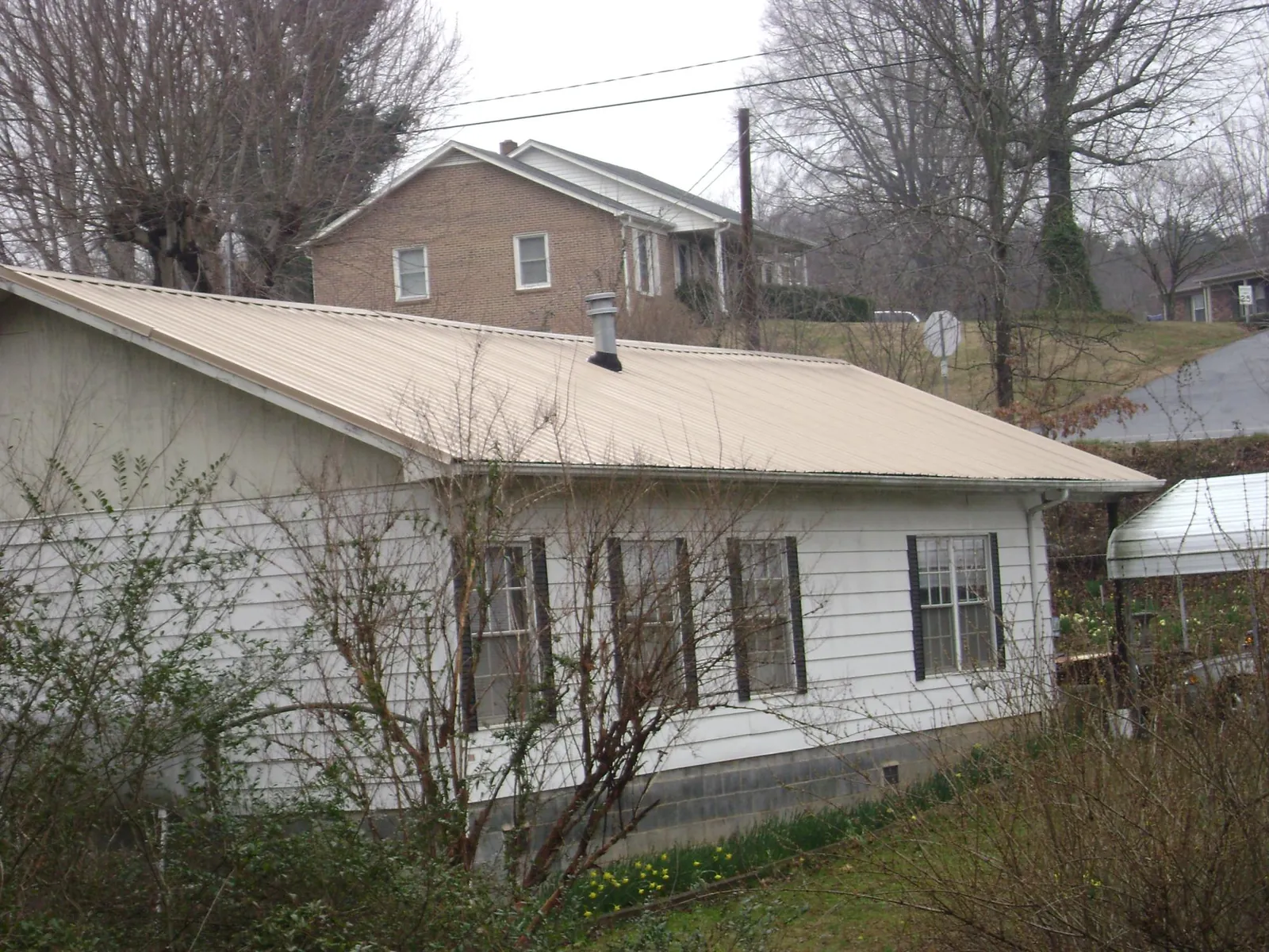 Tan metal roof on a white sided house set into a hillside — Commercial Roofing by Roofing Brothers in Ripplemead